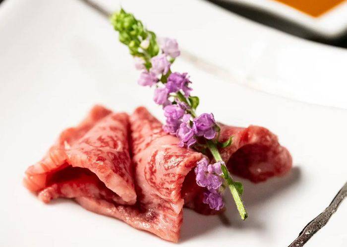 A thinly sliced cut of marbled beef at Wagyu Kappo Toraichi, decorated with edible flowers.
